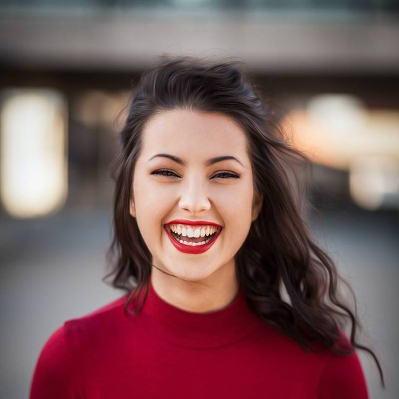 Dunkelhaarige Frau mit roten Lippen lacht, während sie in die Kamera schaut.