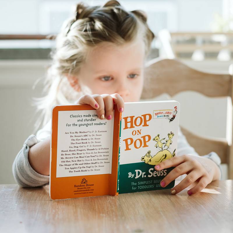 Kleines Mädchen liest ein Buch am Küchentisch.